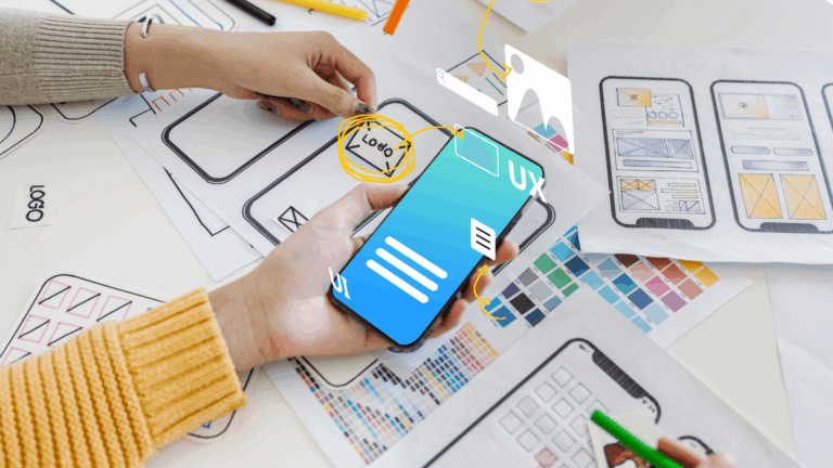 Mani che tengono uno smartphone con grafiche digitali sovrapposte di UI/UX design, su una scrivania piena di bozzetti di app e palette di colori.